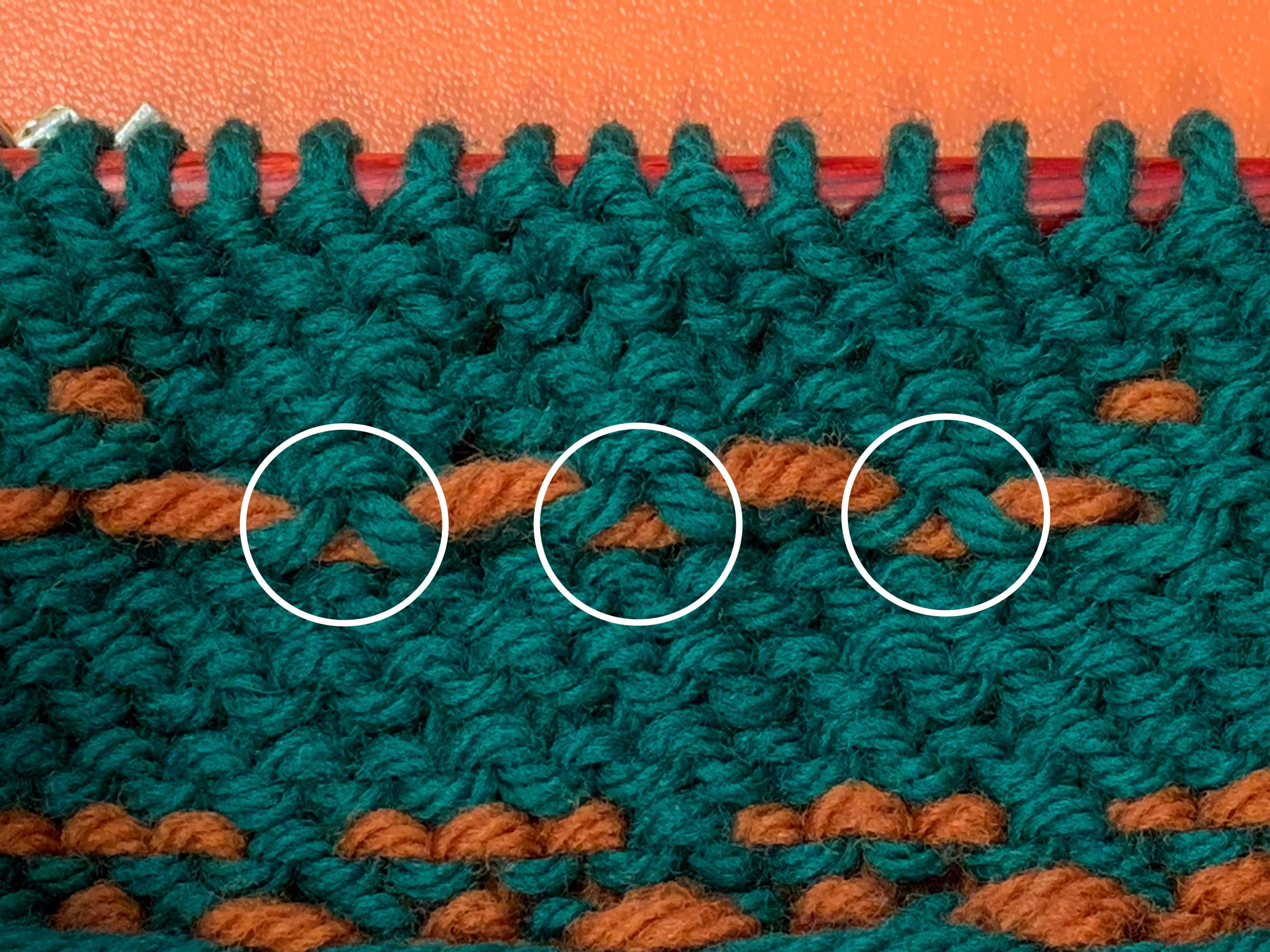A long float of orange yarn that has been caught at three intervals, which are circled in white in the picture.