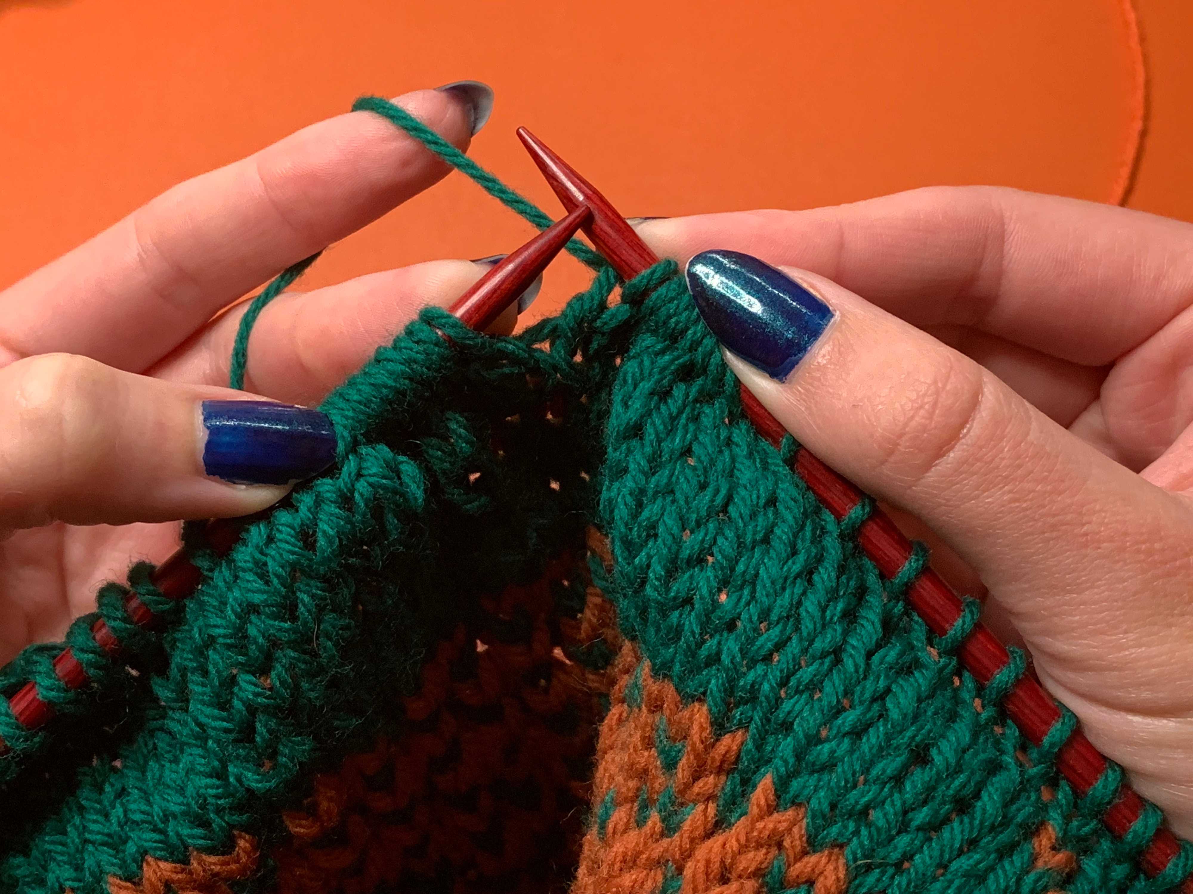 Hands holding a pair of knitting needles. You can see that the stitches are being held very close together on the tips of the needles, but much more spread out the further they get away.