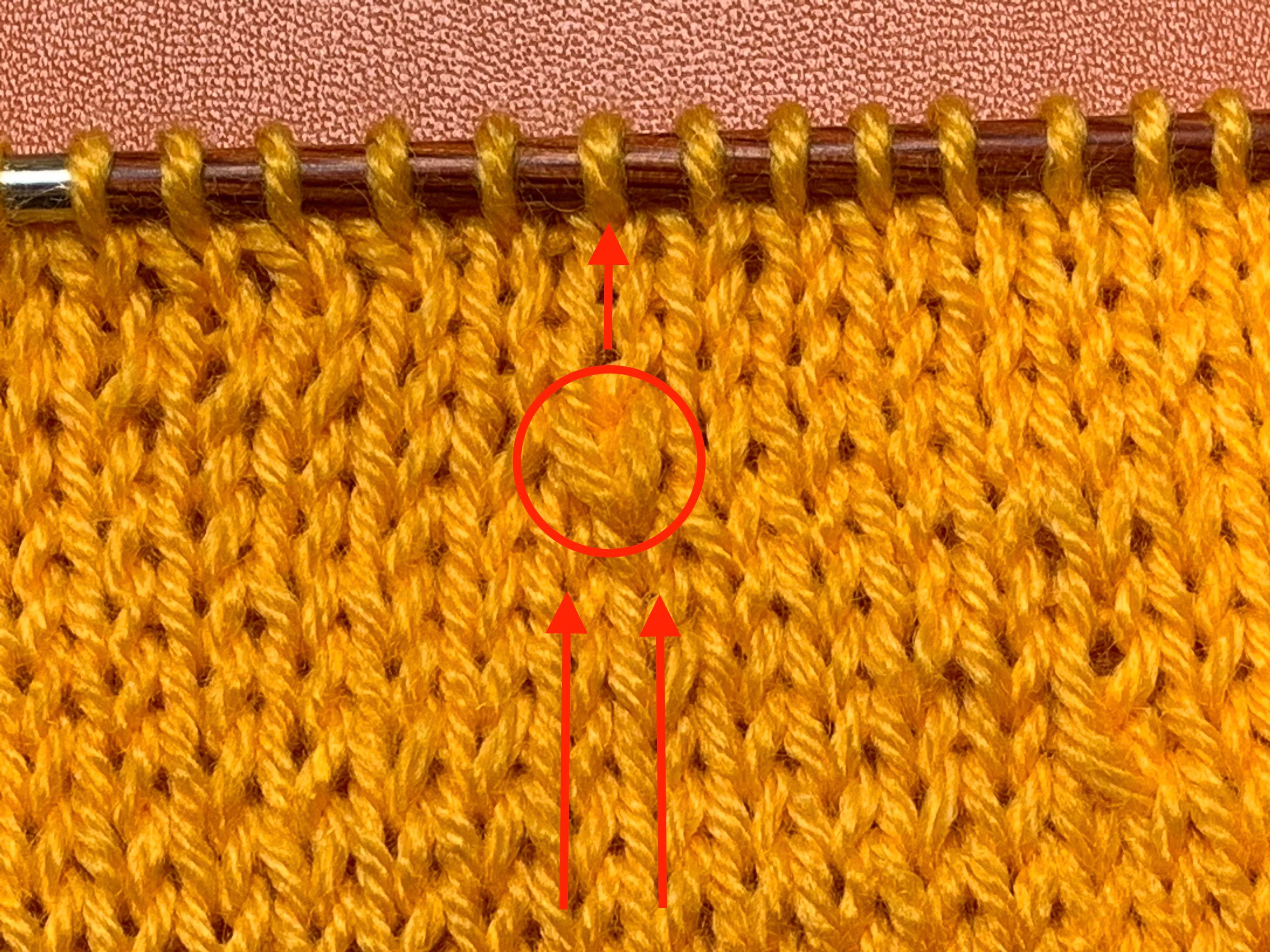 Close-up of an SSK circled in red, with arrows indicating the two stitch columns feeding into the SSK and the single resulting column. If you look closely, you can see that the stitch leans to the left.
